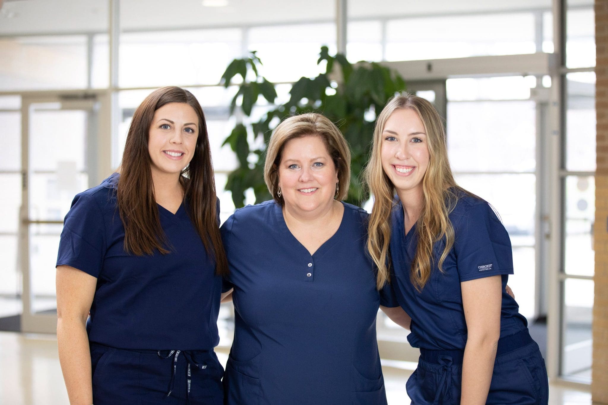 Three friendly healthcare staff members smile warmly by the clinic entrance, ready to welcome individuals with intellectual and developmental disabilities (IDD), including Autism Spectrum Disorder (ASD), Down Syndrome, and Cerebral Palsy, for specialized medical, therapy, and behavioral health services.