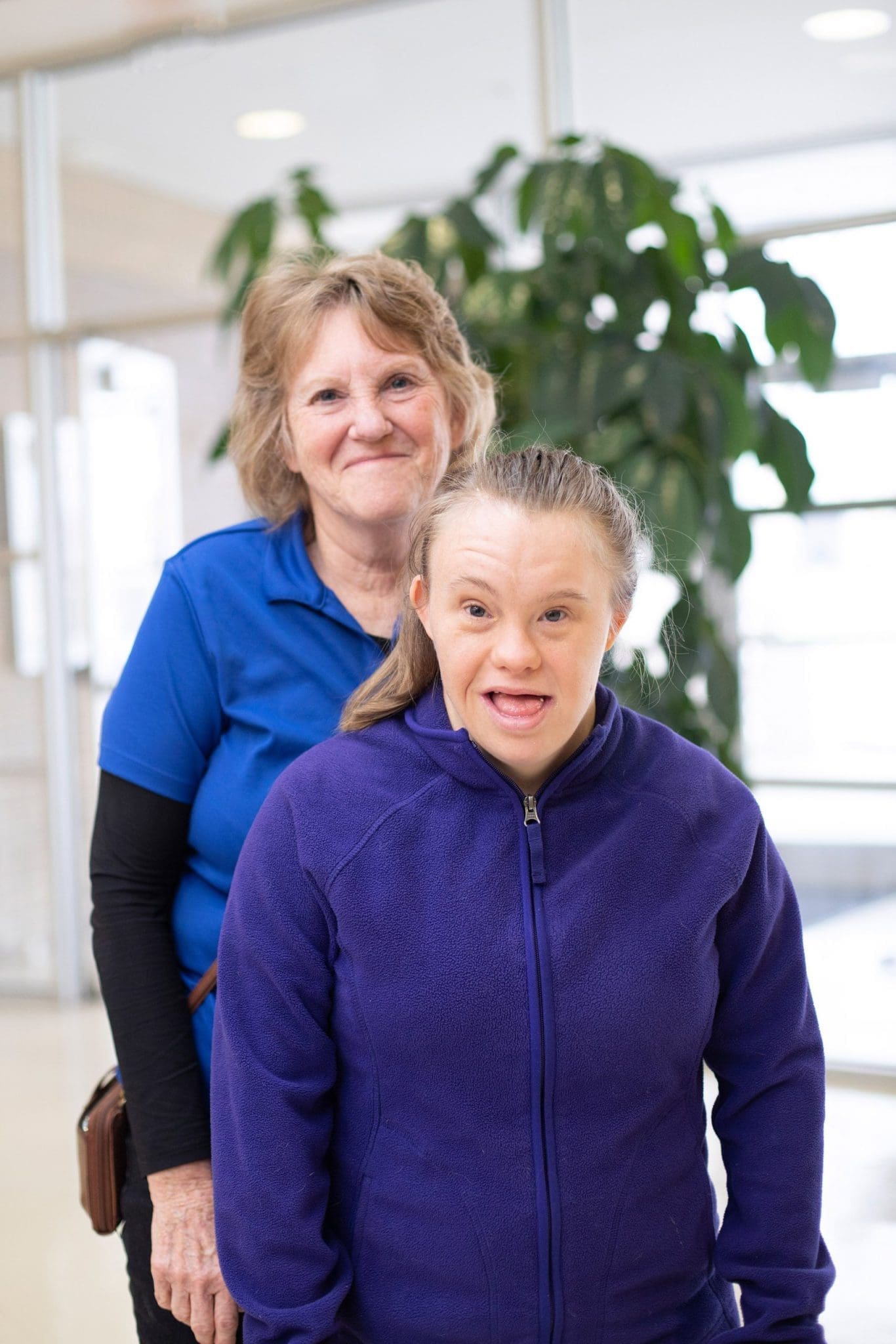 Mother and daughter with Down syndrome stand by the clinic doors, smiling after a successful day of comprehensive, integrated healthcare appointments.