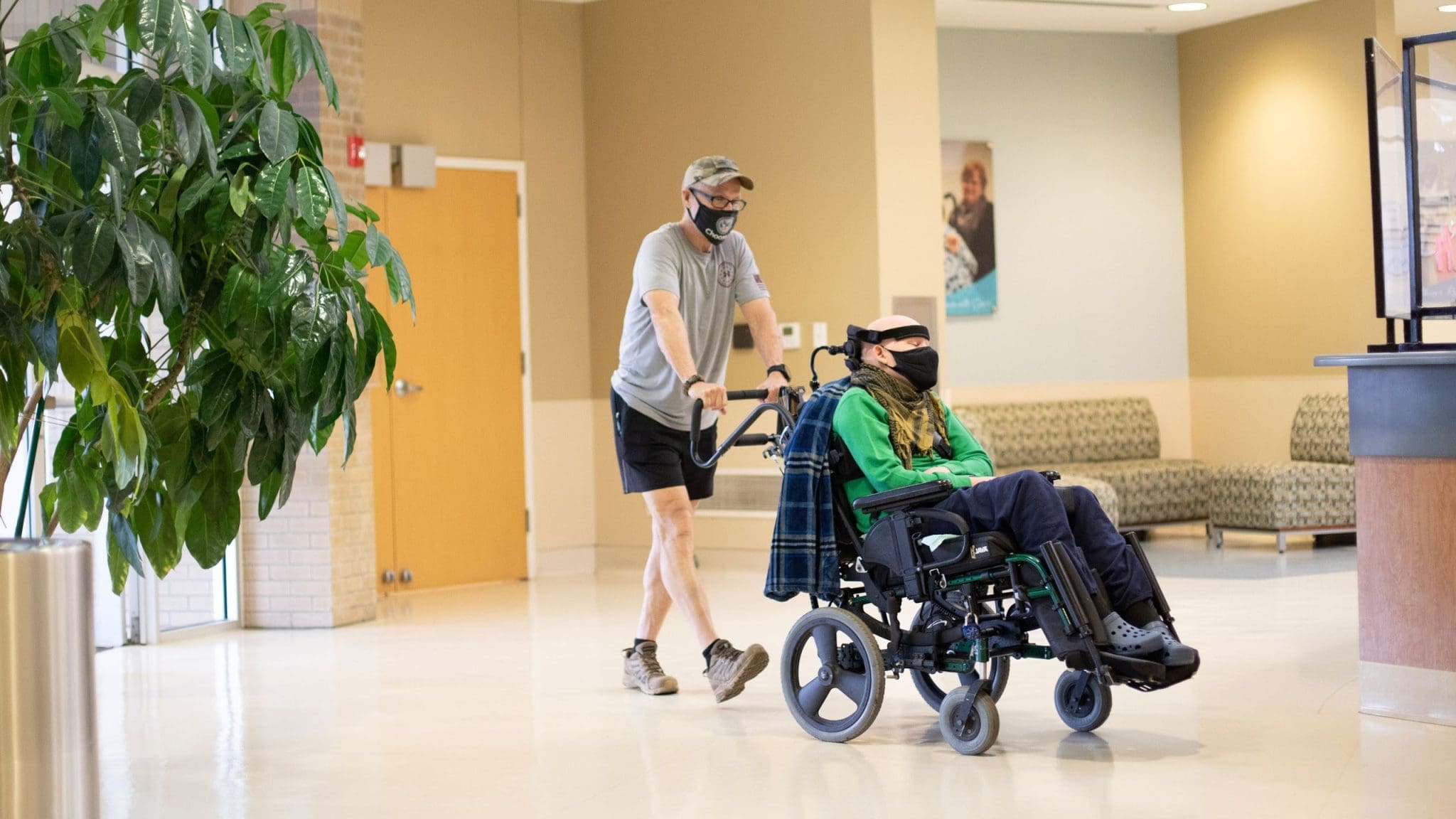 Caregiver assisting a young man in a wheelchair as they enter the Lee Specialty healthcare clinic, ensuring accessibility and inclusive care.