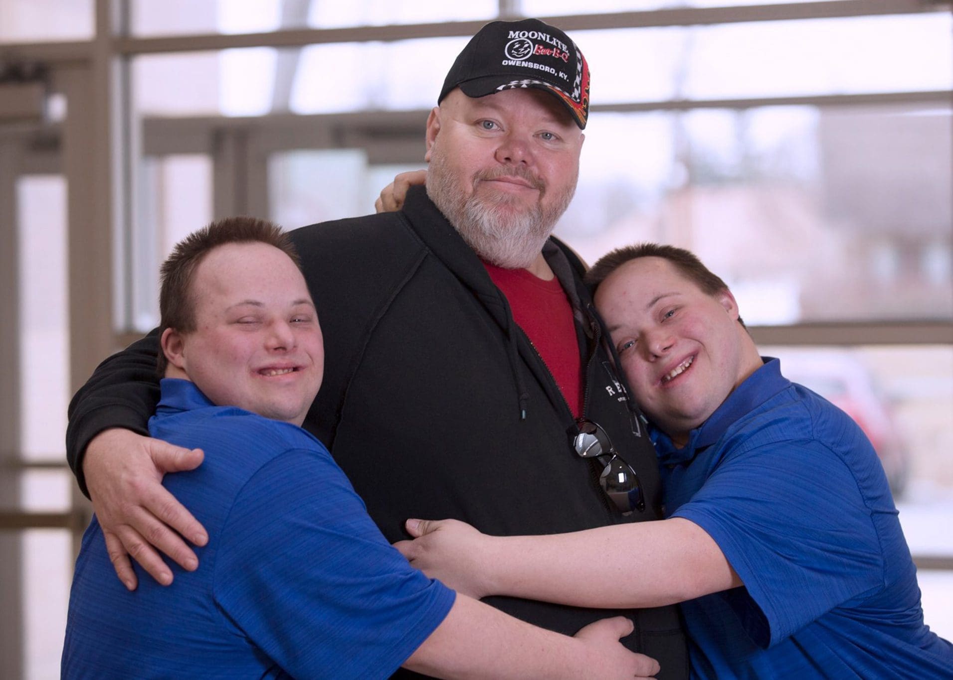 Father embraced by his twin sons with Down syndrome, celebrating family support and quality healthcare for individuals with intellectual and developmental disabilities (IDD).