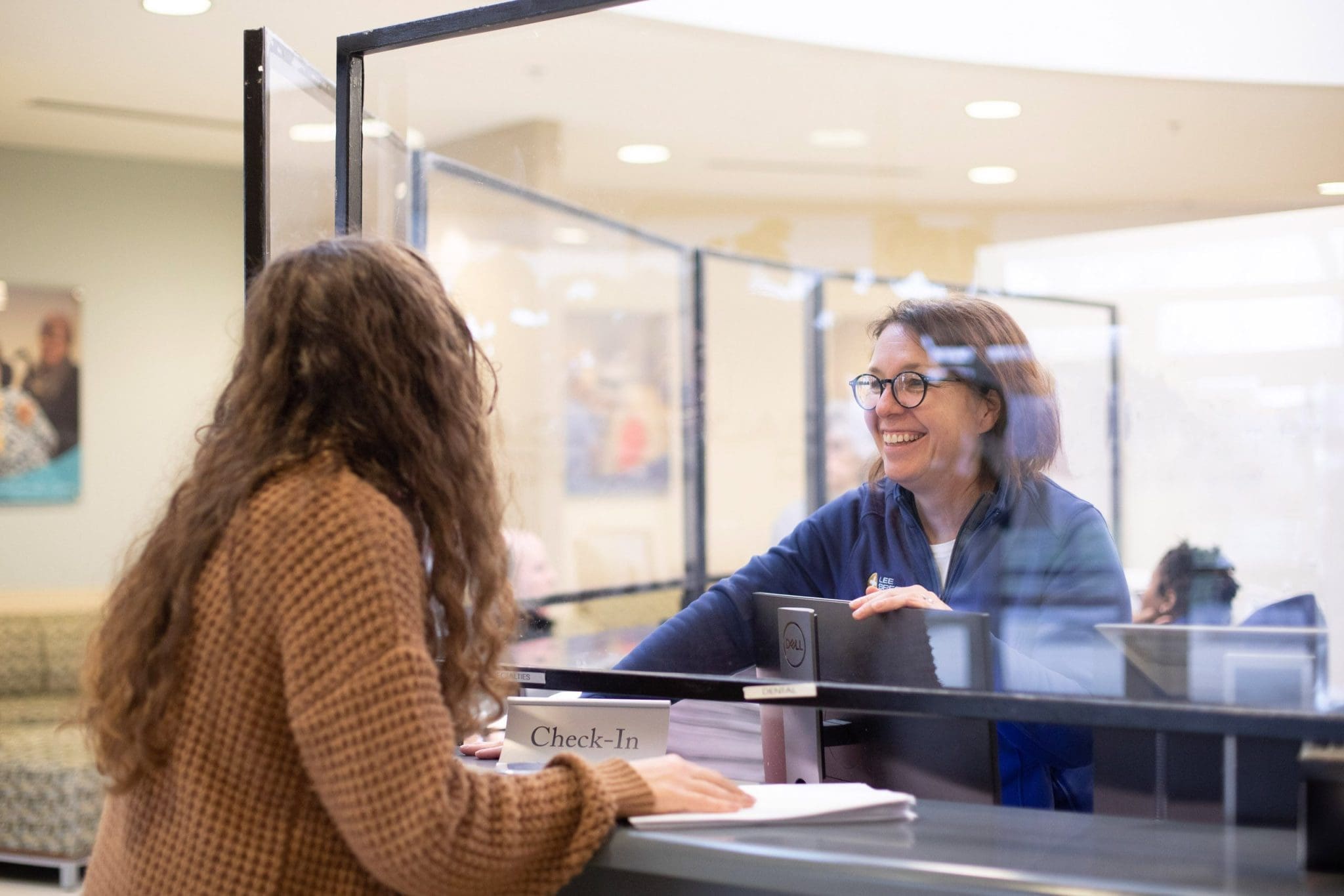 Patient with Global Developmental Delay (GDD) standing at the welcome desk while a smiling receptionist assists her.