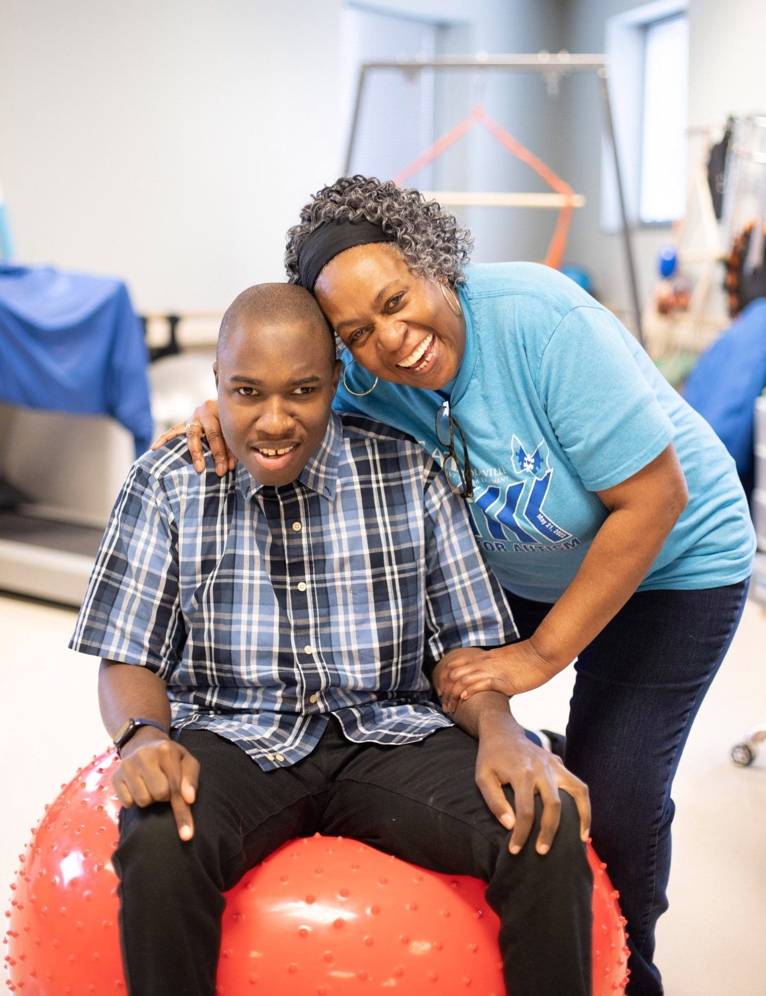 Tina Davis puts her arm around her non-verbal son, Terrence Davis as he bounces on a bright red therapy ball.