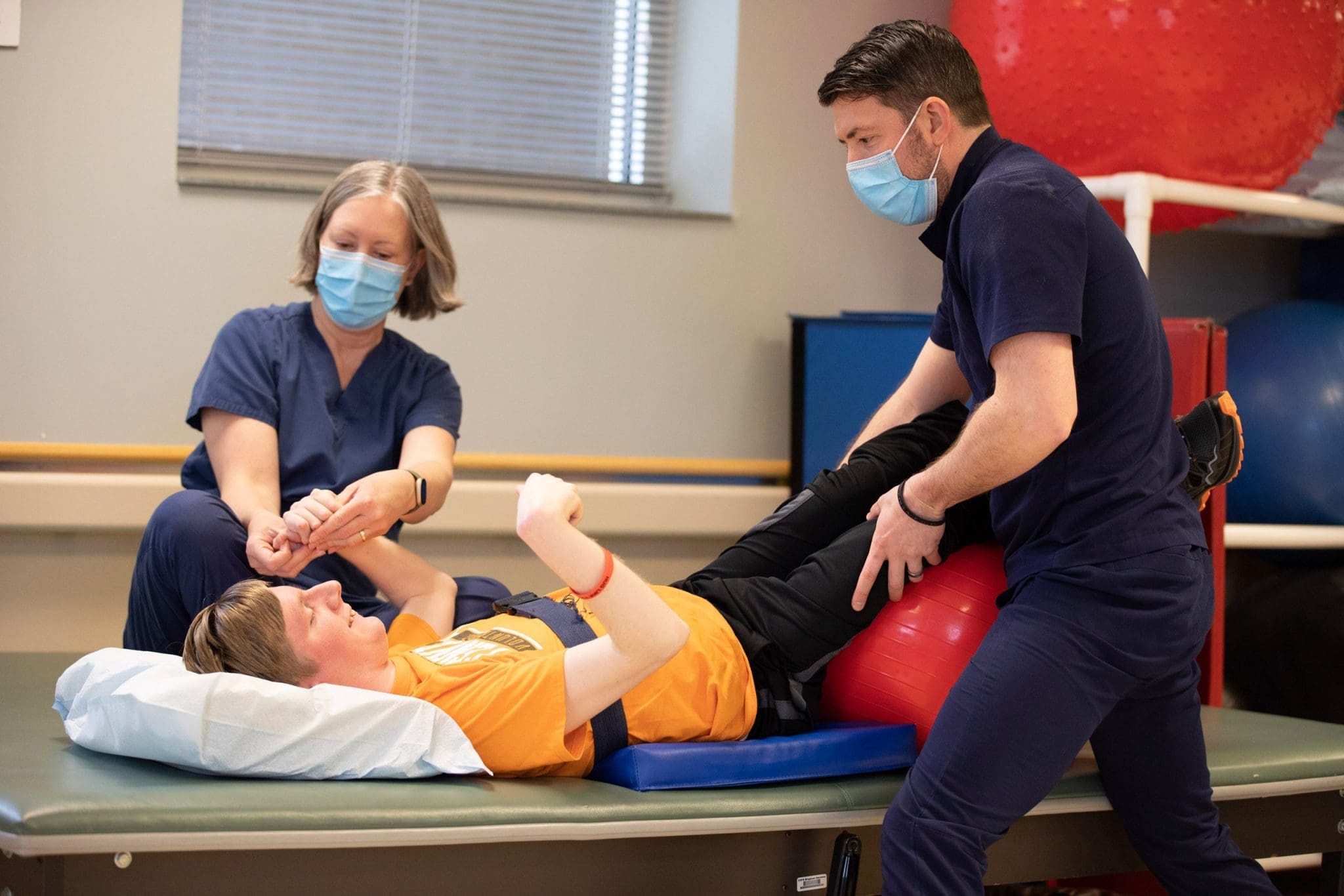 Therapists assist a patient with cerebral palsy in guided stretching exercises to improve mobility, flexibility, and muscle strength.