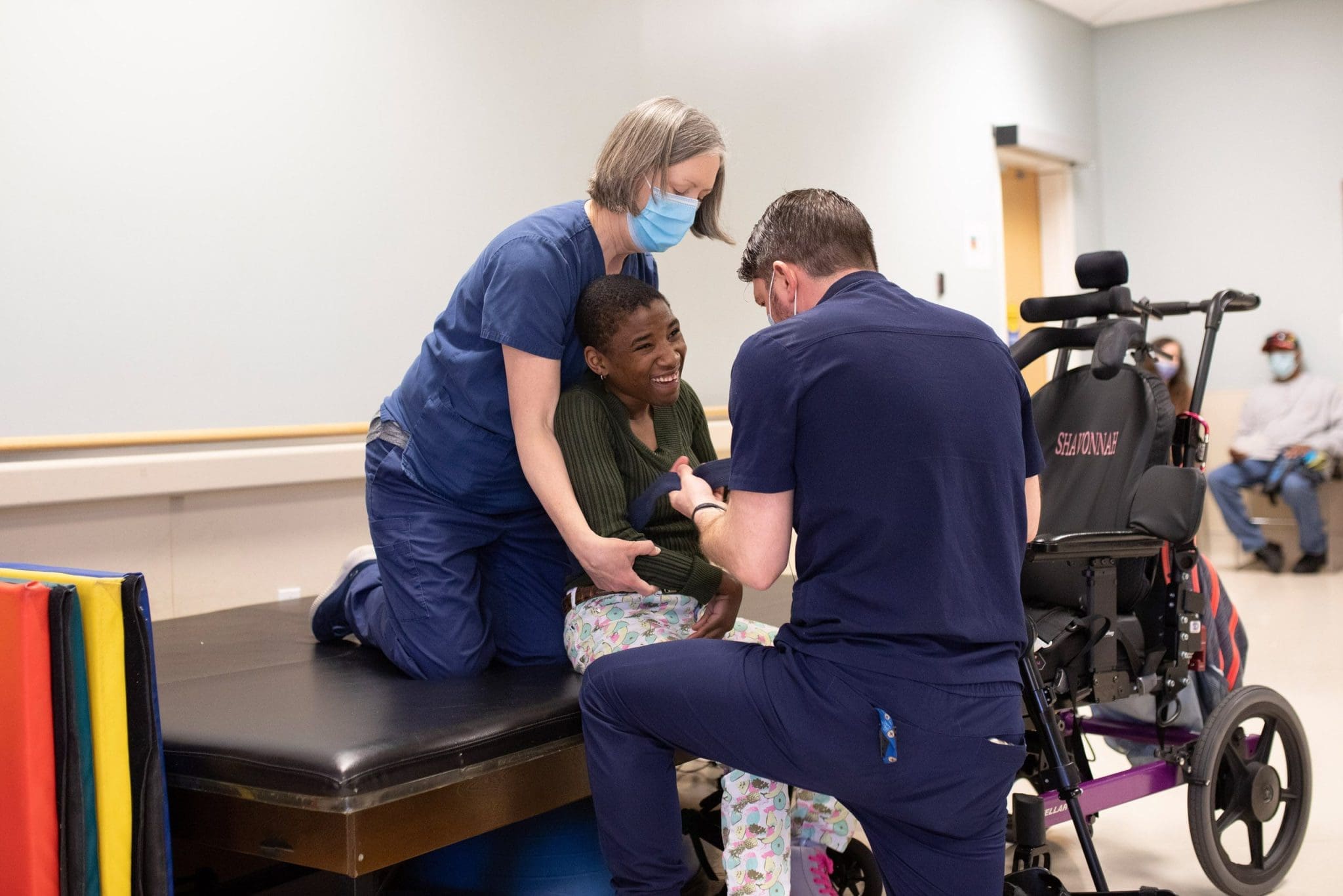 Two physical therapists assist a patient with intellectual and developmental disabilities (IDD) in preparing for walking exercises, focusing on mobility, strength, and independence in a supportive rehabilitation setting.