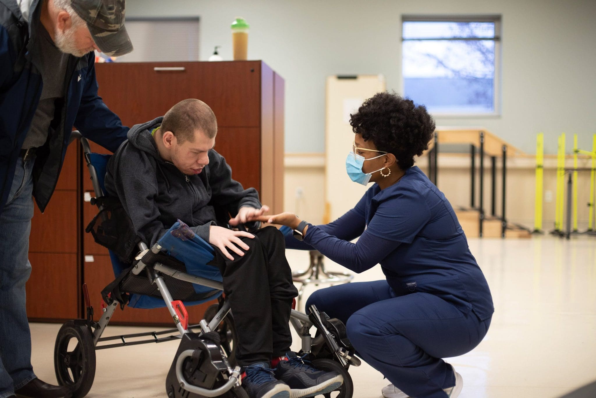 Therapist gently communicates with a man with intellectual and developmental disabilities (IDD) in a wheelchair, preparing him for his appointment in a supportive and sensory-friendly healthcare environment.