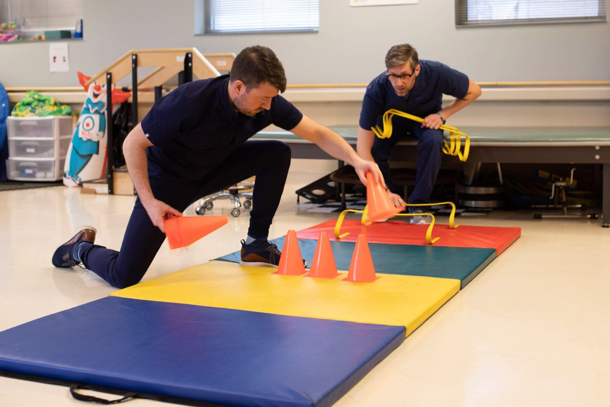 Two therapists set up a dynamic obstacle course to support mobility, coordination, and balance training for patients with intellectual and developmental disabilities (IDD) in a physical rehabilitation session.