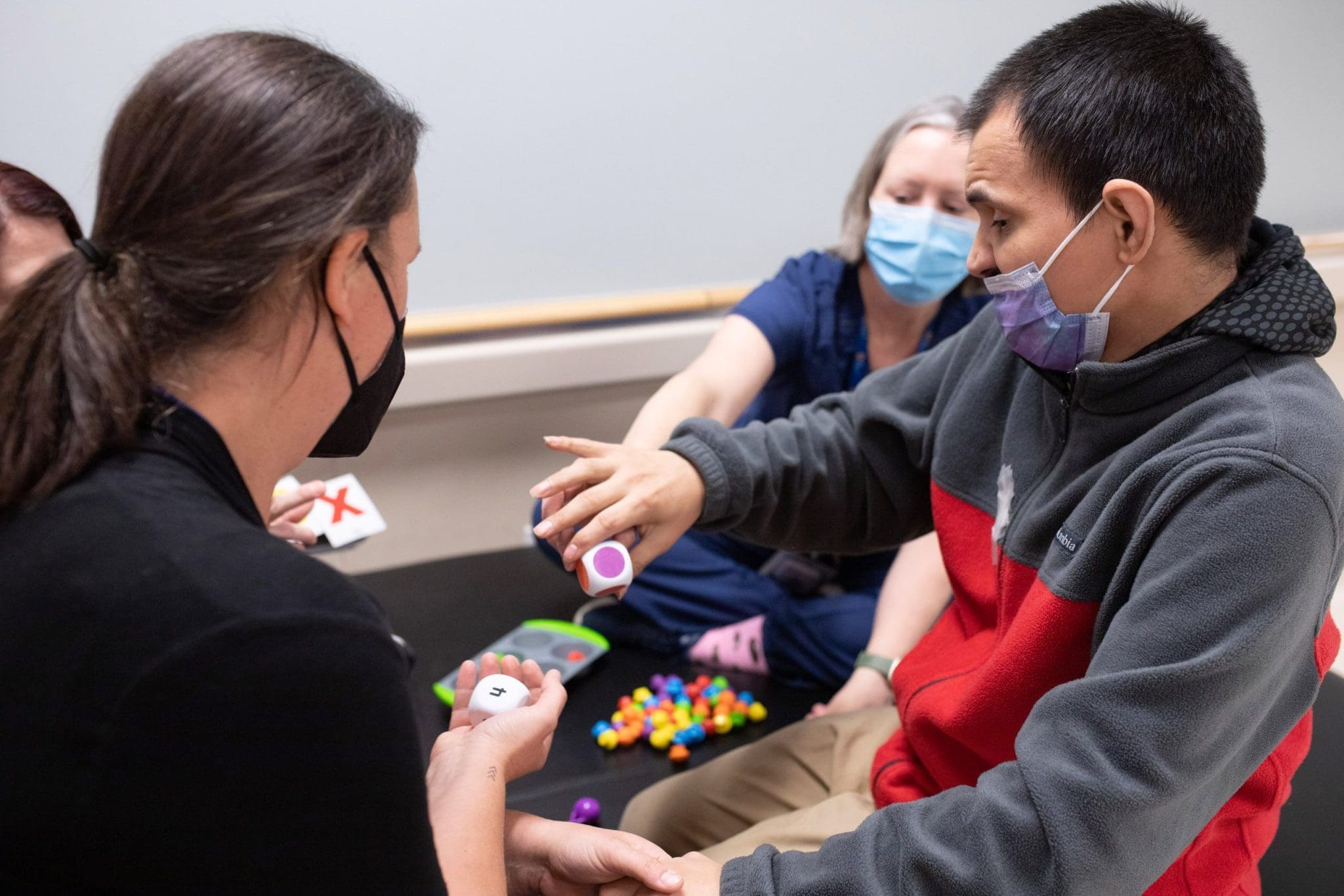 Psychiatrist collaborates with two therapists and a caregiver to support a man with an Intellectual and Developmental Disability in a coordination exercise using shapes, colors, and small objects.