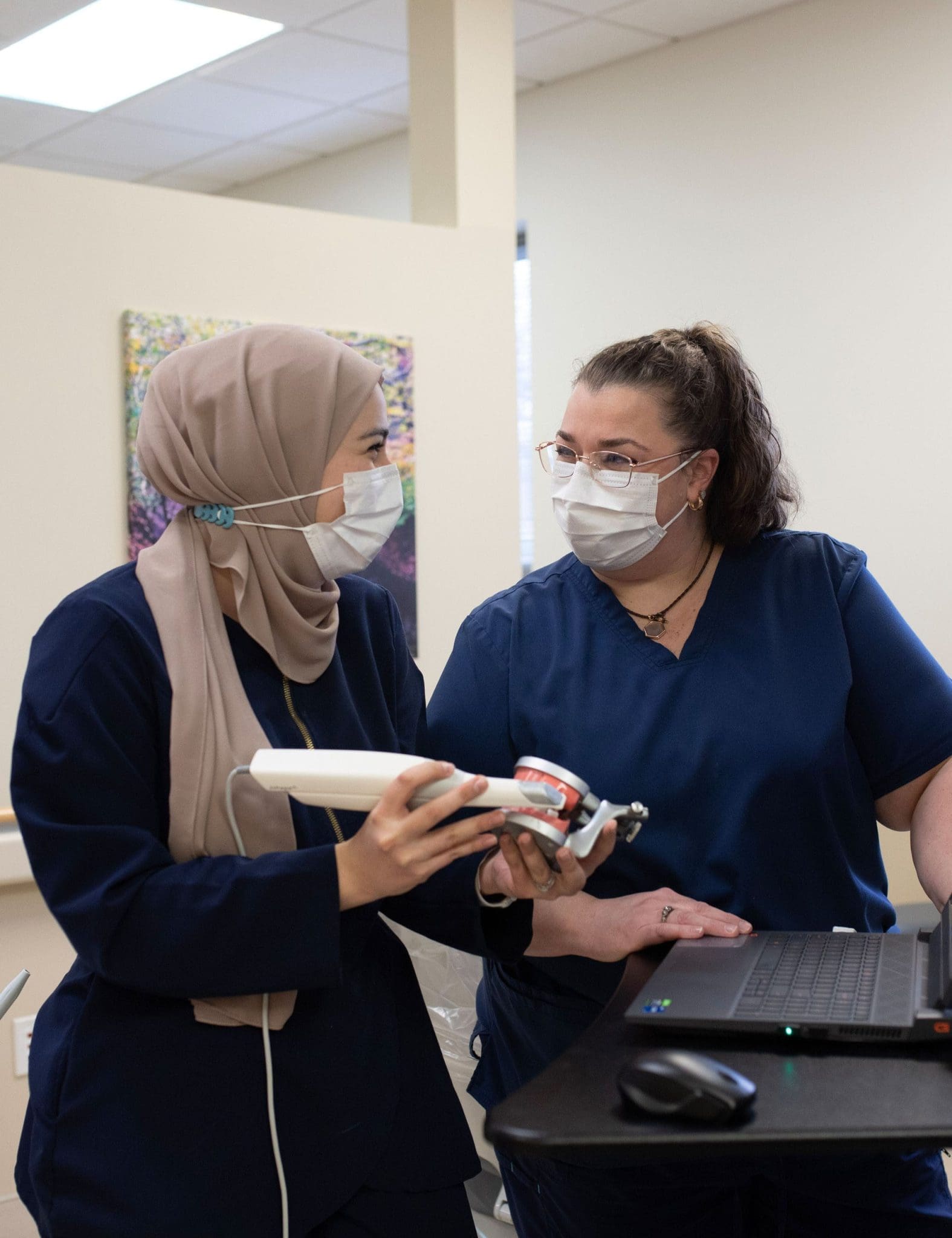 Dentist instructs dental student on proper use of advanced dental scanning equipment for patient care.