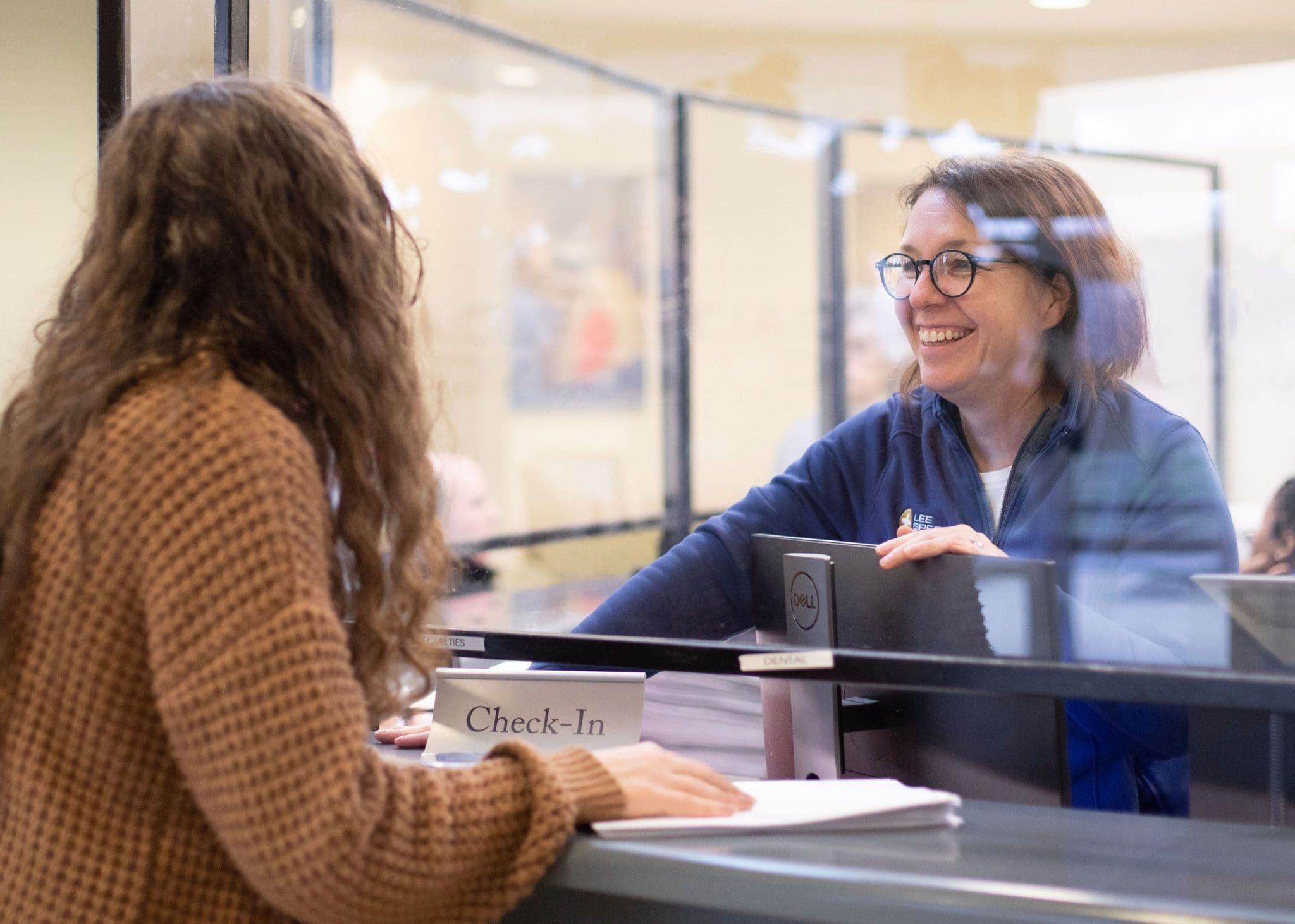 Patient with Autism Spectrum Disorder standing at the welcome desk while a smiling receptionist assists her with paperwork at our specialized healthcare clinic.