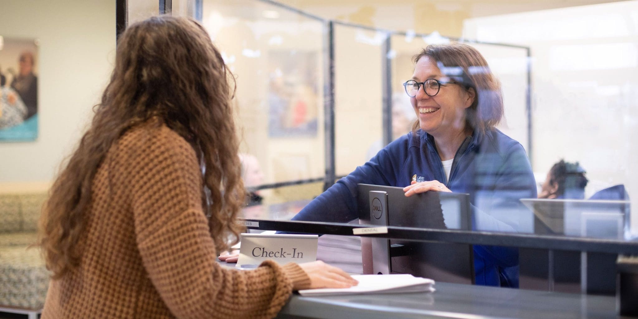 Patient with Global Developmental Delay (GDD) standing at the welcome desk while a smiling receptionist assists her.