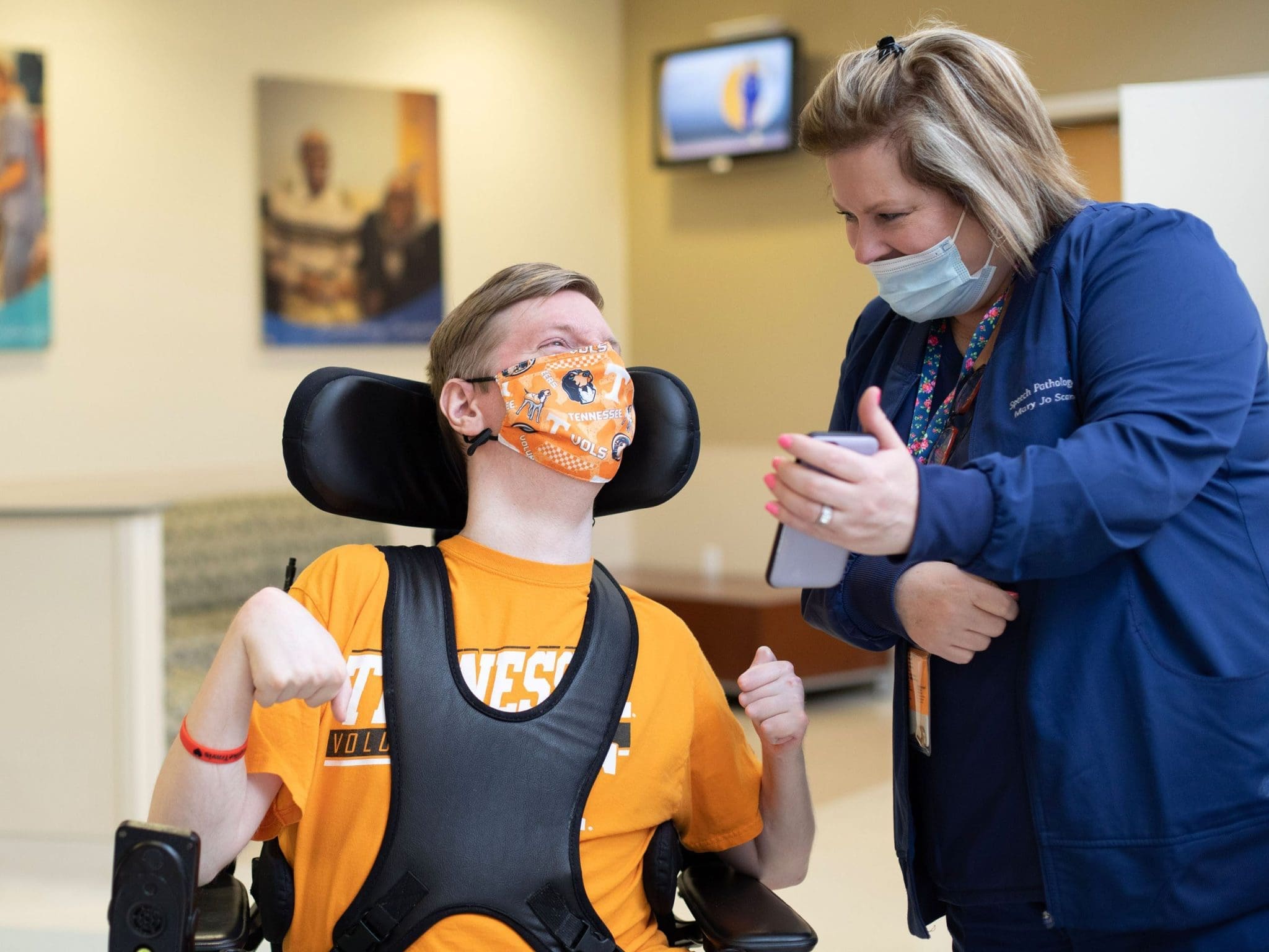 Nurse showing a funny picture to a young man in a wheelchair, creating a positive and inclusive healthcare experience.