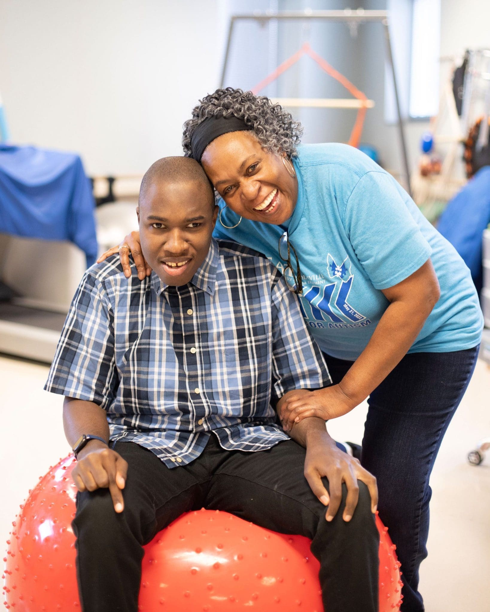Tina Davis embraces her non-verbal son, Terrence, as he engages in sensory therapy on a bright red therapy ball.
