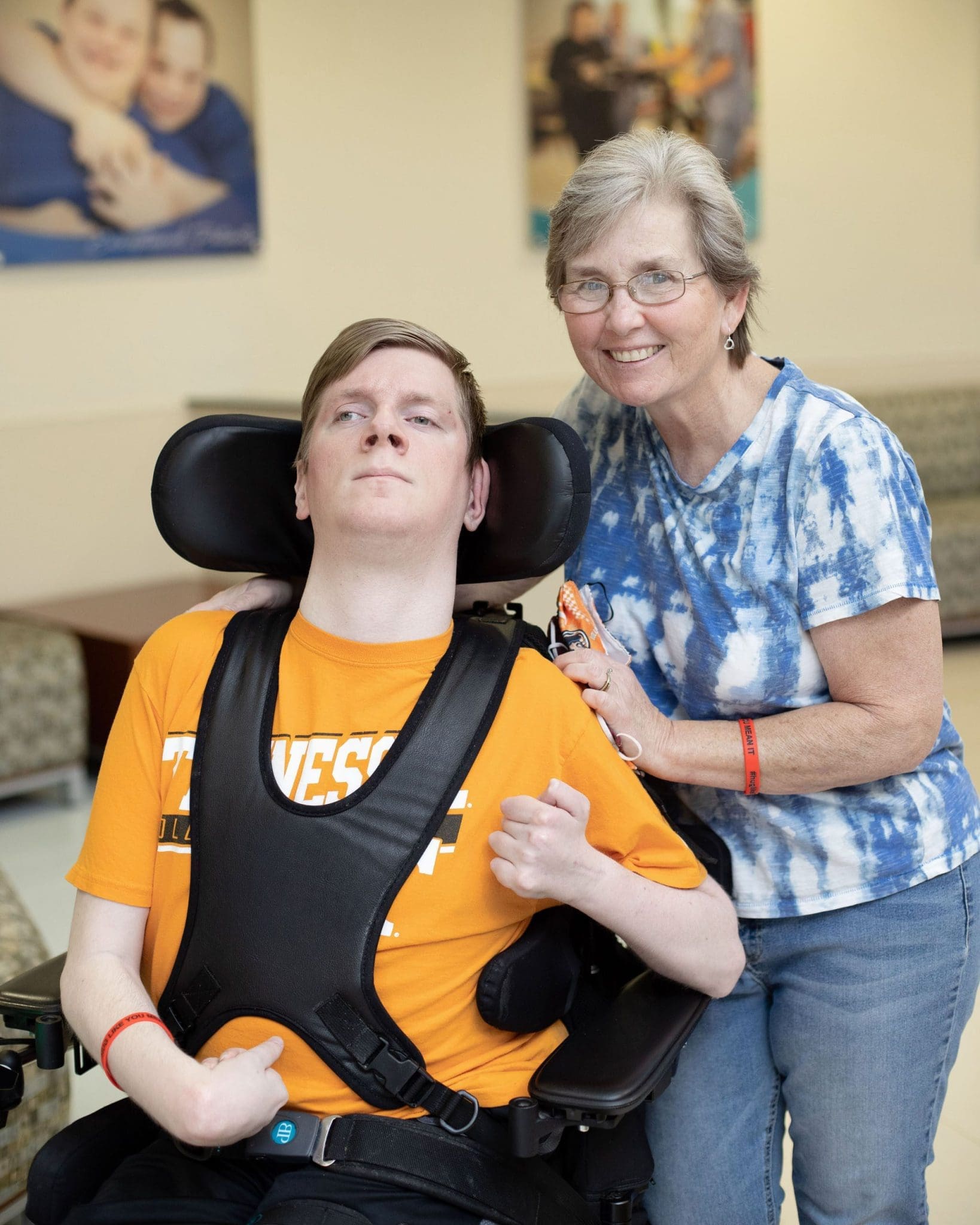 Mother (Rita), stands with her hand on the shoulder of her son, Dustin who is seated in a wheel chair.