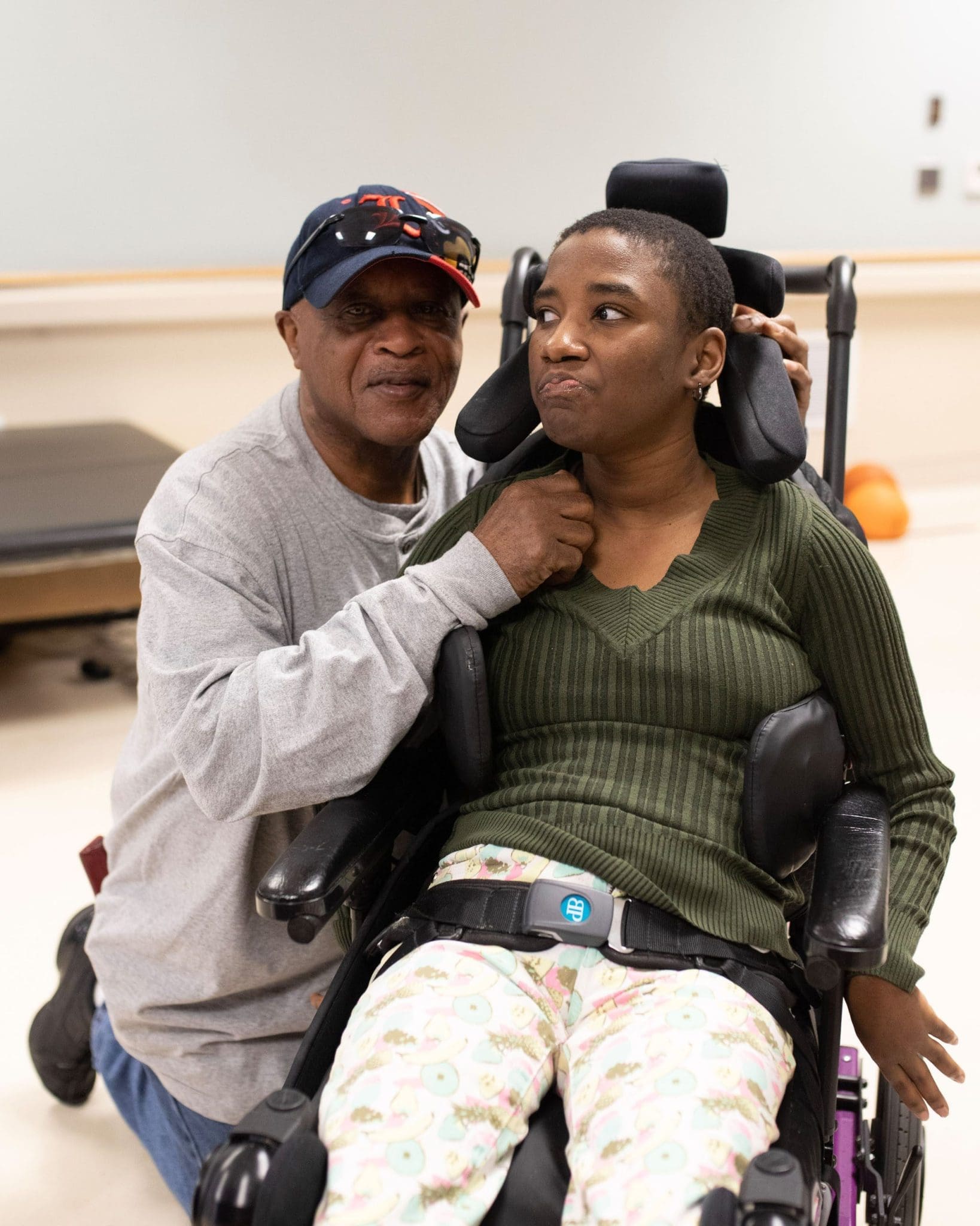 A father sits beside his daughter, who uses a wheelchair, as they await her physical therapy appointment.