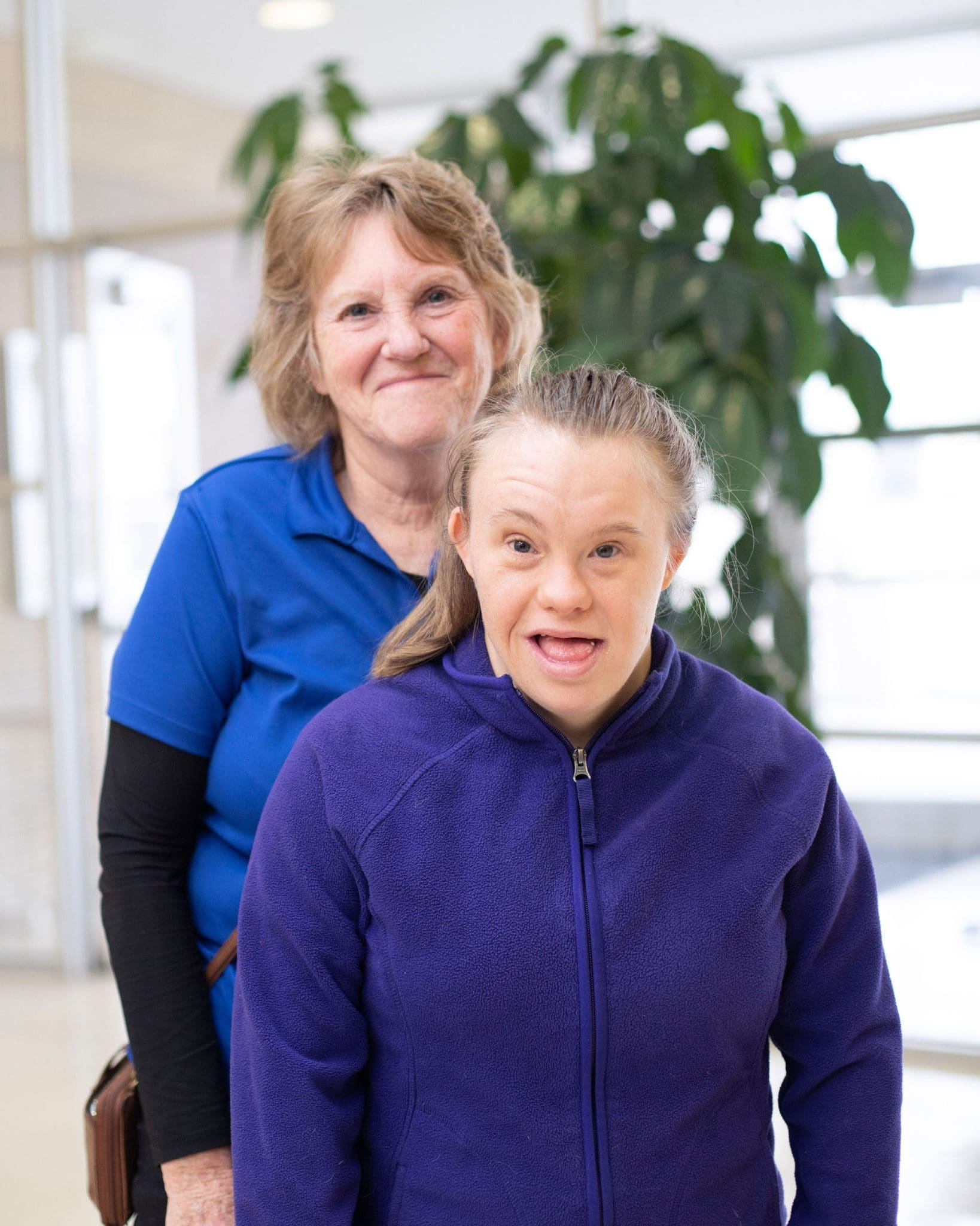 A smiling mother stands with her young daughter, who has Down syndrome, as they enjoy a moment together.