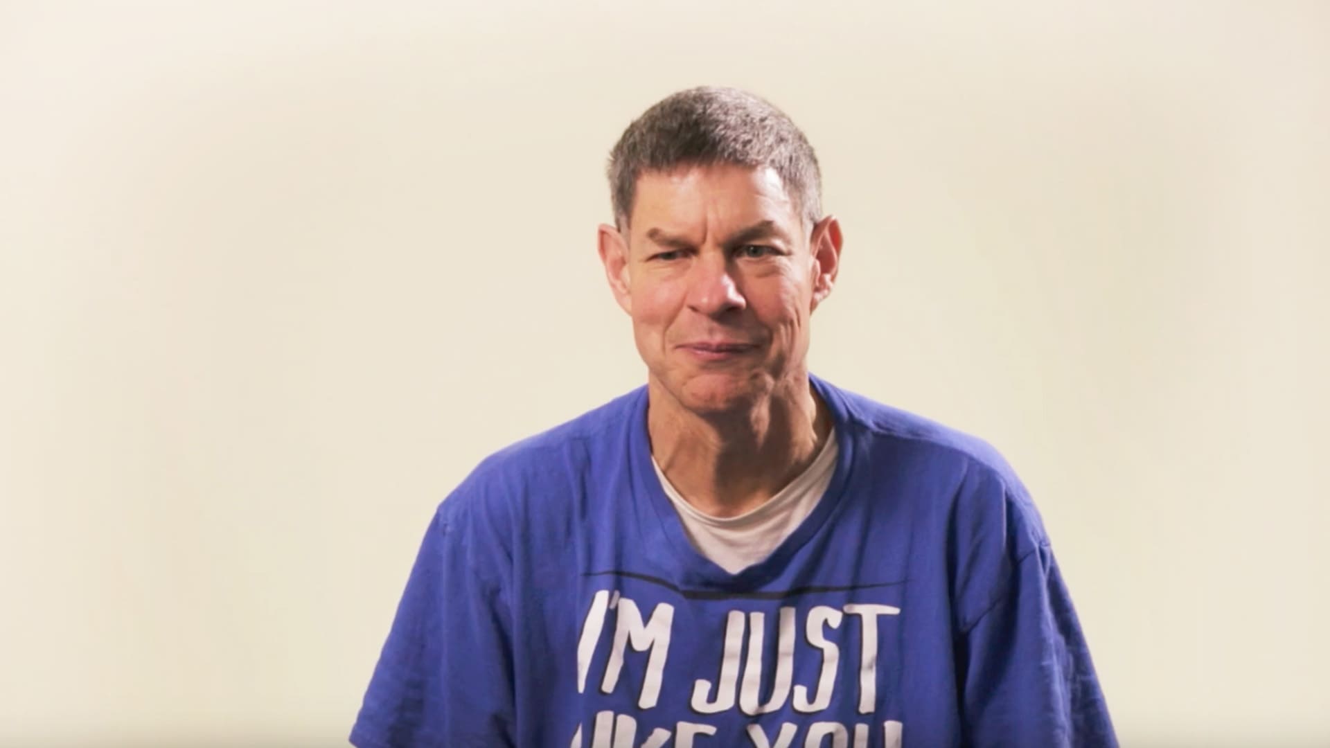 person wearing a blue shirt with text speaking against a plain background