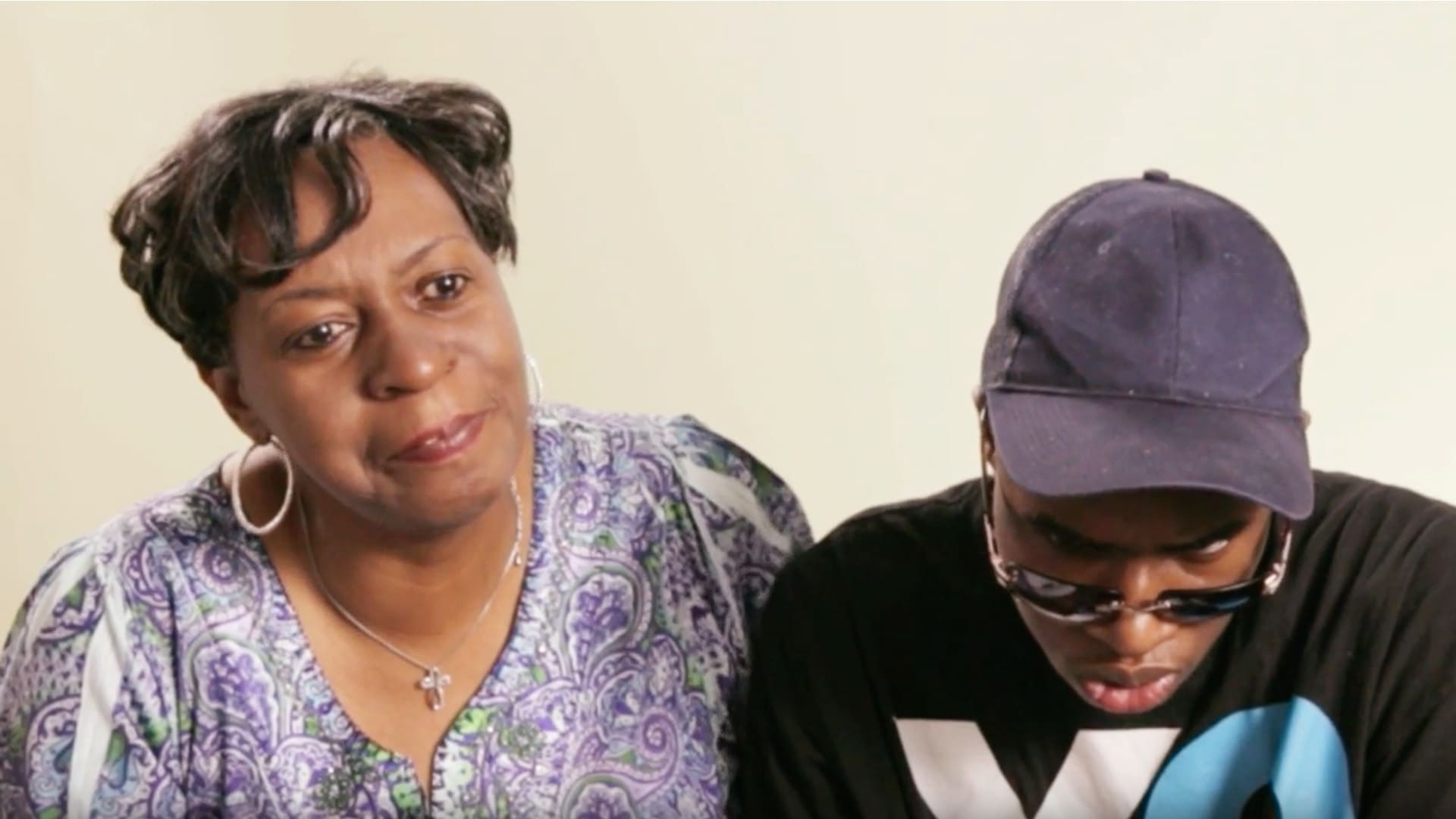 Two people sitting closely, one wearing a patterned top and the other wearing a cap and sunglasses